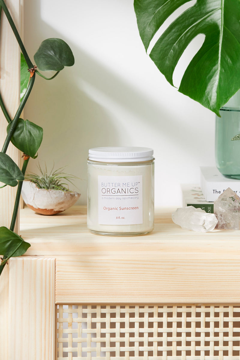 Non-nano zinc oxide sunscreen jar on wooden shelf, surrounded by plants and crystals.