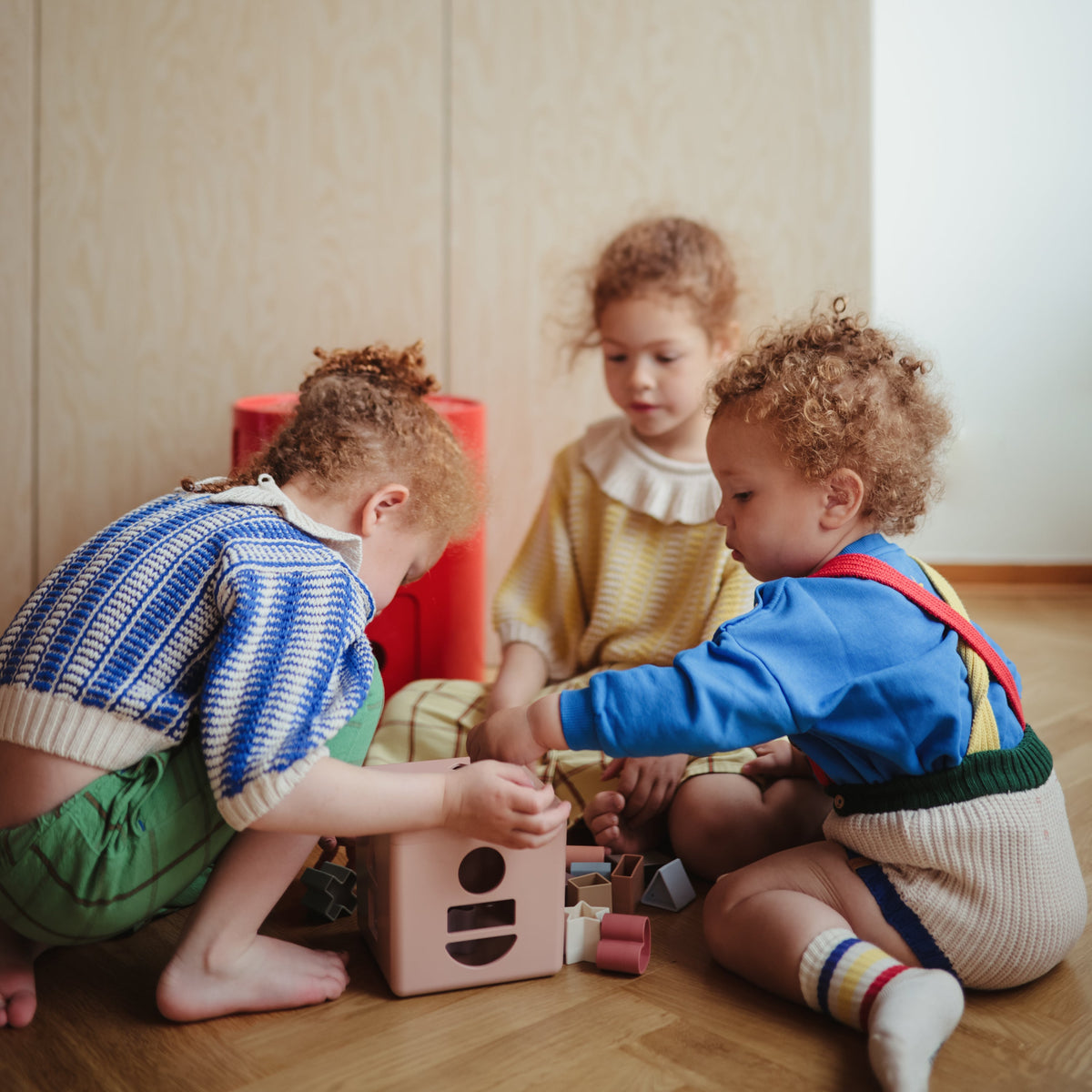 Mushie natural wood shape sorting box with colorful geometric shapes for babies.