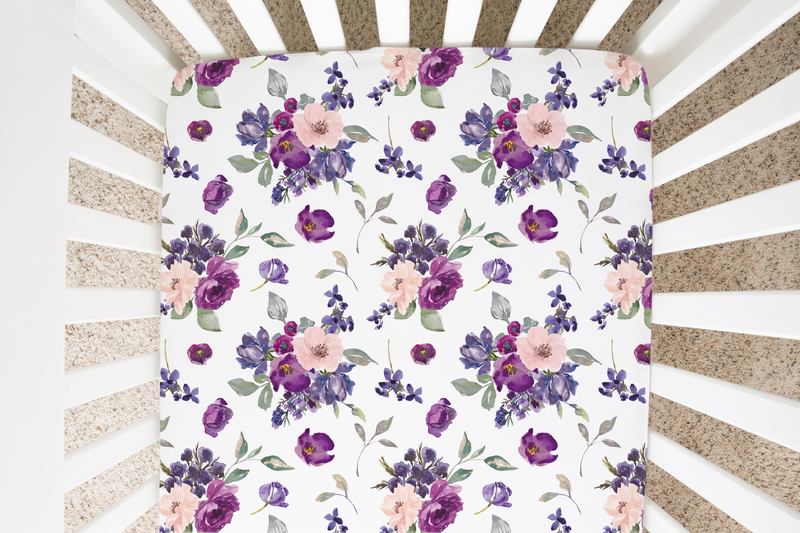 Purple and blush floral fitted crib sheet in a white crib.