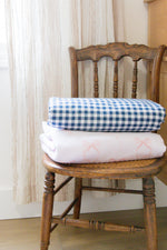 Little Mae & Co organic navy gingham quilted crib blanket draped over a white crib.
