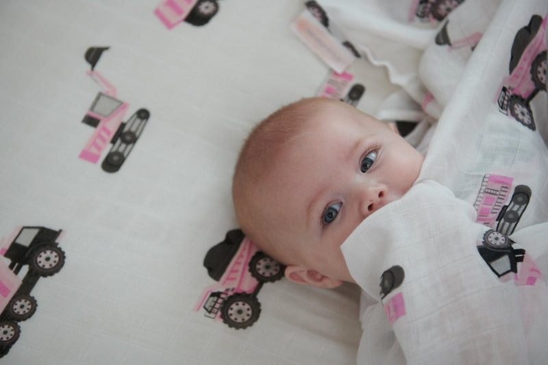 Baby lying on a pink digger themed bamboo crib sheet; soft, breathable, and snug fit for standard crib mattresses.