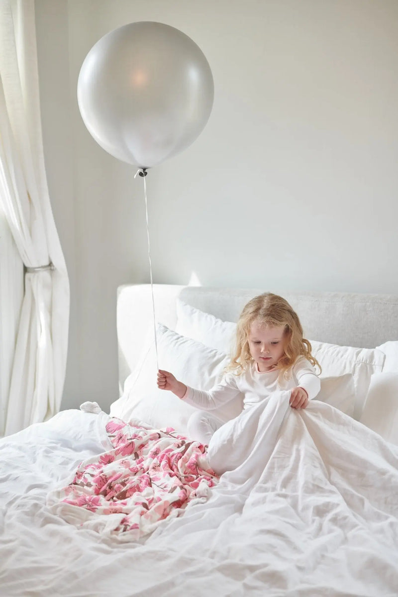Cherry Blossom Bamboo Muslin Newcastle Blanket with a pink floral design on a bed.