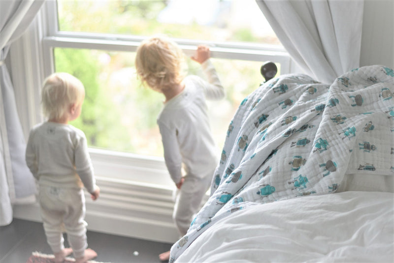 Robots Cotton Muslin Newcastle Blanket draped on bed with children by window.