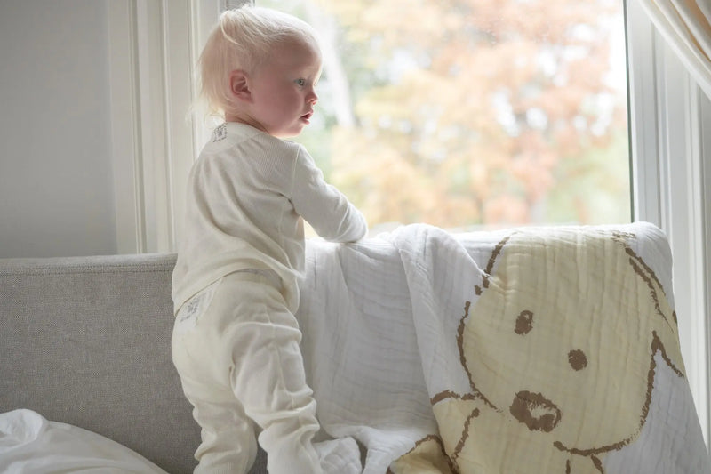 Child with Teddy Bear and Plaid Cotton Muslin Newcastle Blanket on sofa.