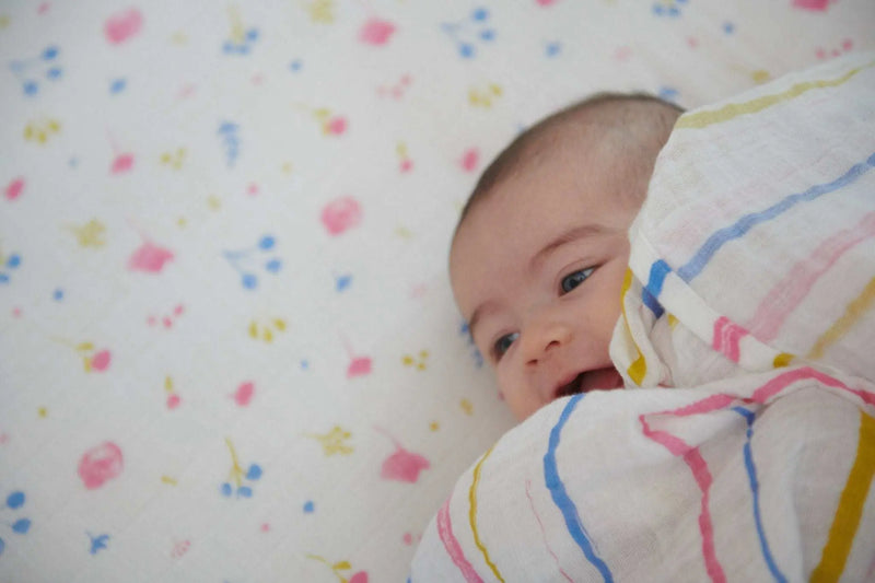 Baby wrapped in watercolor stripe cotton muslin swaddle blanket.