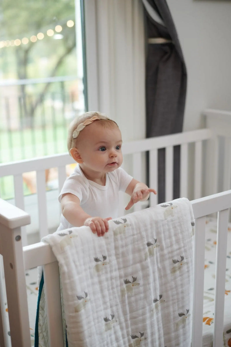 Baby with Mister Moose and Forest Arrow cotton muslin blanket in crib.