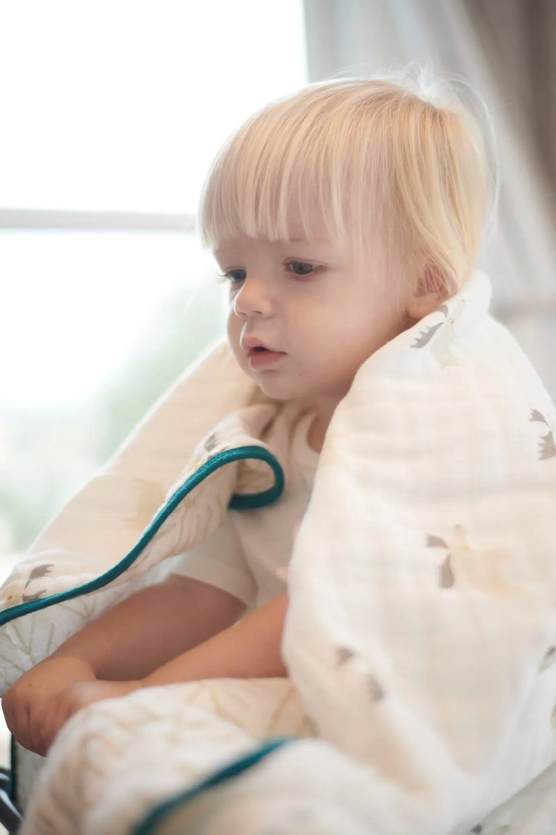 Child wrapped in soft Mister Moose and Forest Arrow cotton muslin blanket.