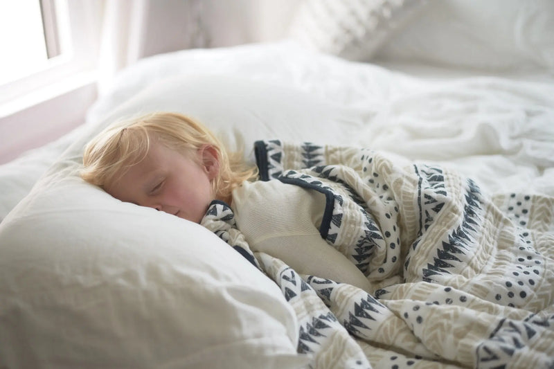 Child snuggled under Pyramid Cotton Muslin Newcastle Blanket on a white bed.