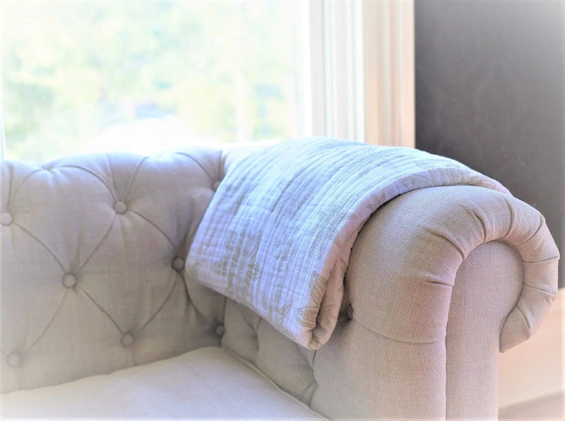 Boho Fields Cotton Muslin Newcastle Blanket draped over a sofa, showcasing its soft, breathable natural cotton fibers.