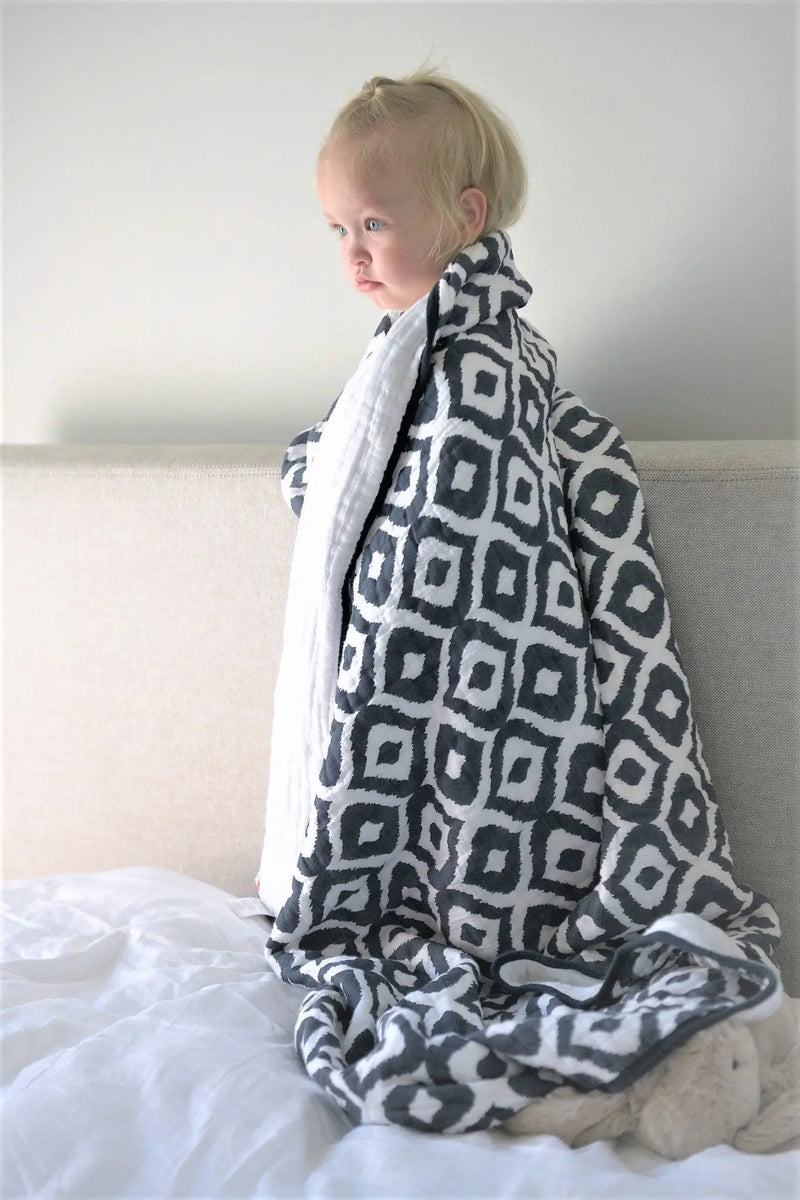 Toddler wrapped in Moroccan Blue Cotton Muslin Newcastle Blanket on a bed.