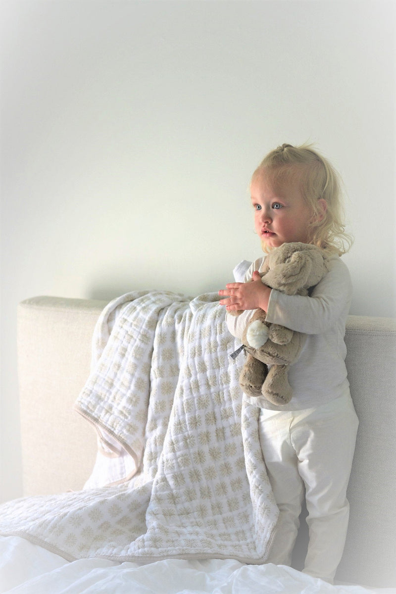 Flower Child Cotton Muslin Newcastle Blanket on bed with toddler holding stuffed animal.