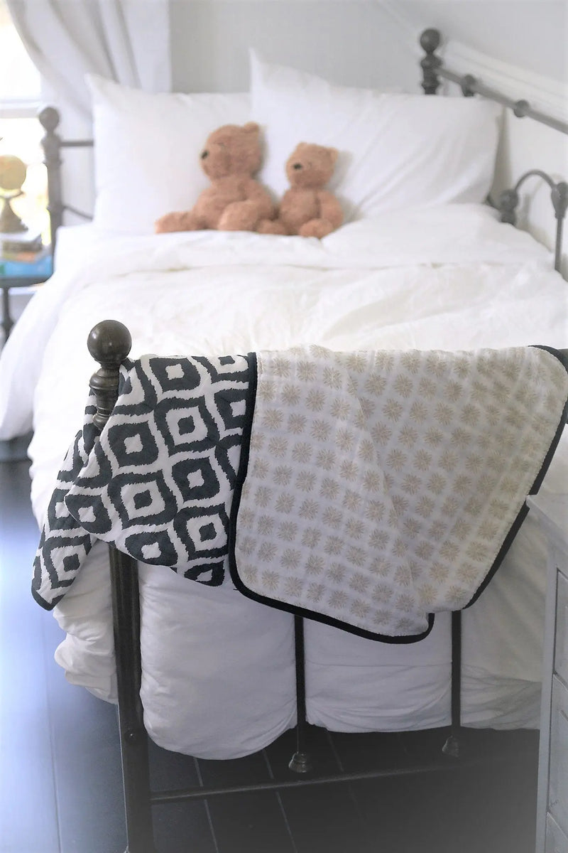Morrocan Blue And Flower Child cotton muslin blanket draped over a bed, featuring a soft, cozy four-layer design.