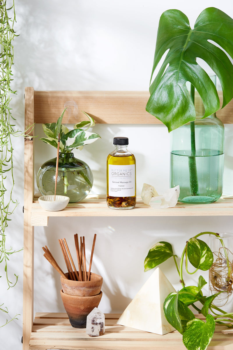 Sensual massage oil bottle on wooden shelf with plants and natural decor.