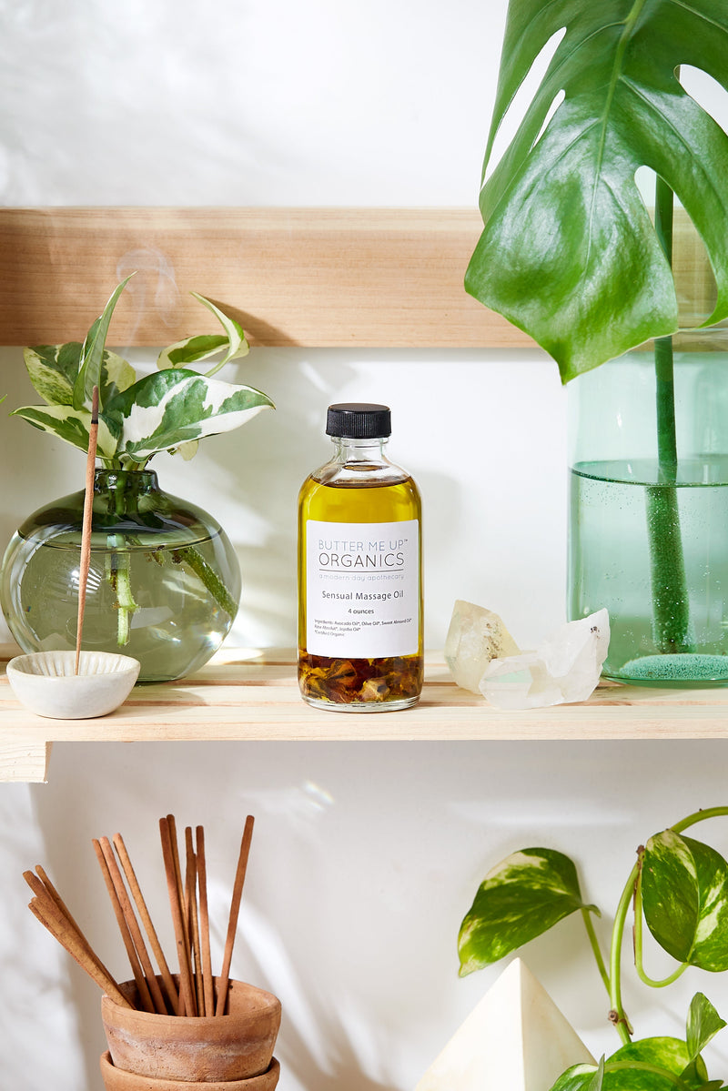 Organic sensual massage oil bottle on a shelf with plants, offering smooth glide and rose scent.