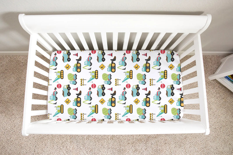Fitted crib sheet with construction truck pattern in a white crib.