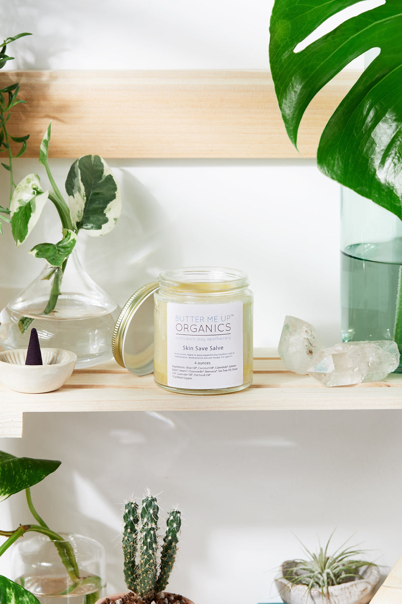 Skin Save Salve jar on a wooden shelf surrounded by plants and crystals.