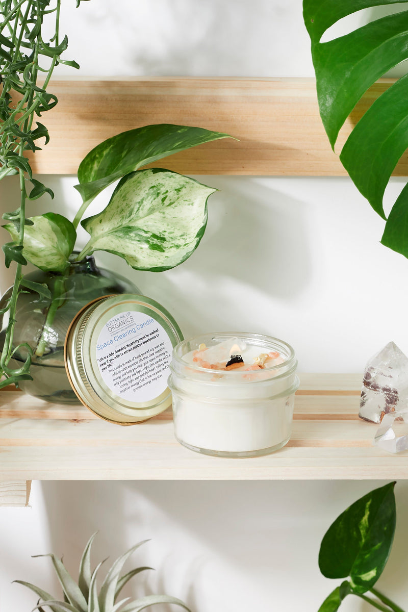 Organic soy space clearing candle with crystals, on a wooden shelf with greenery, designed for energy cleansing and intention setting.
