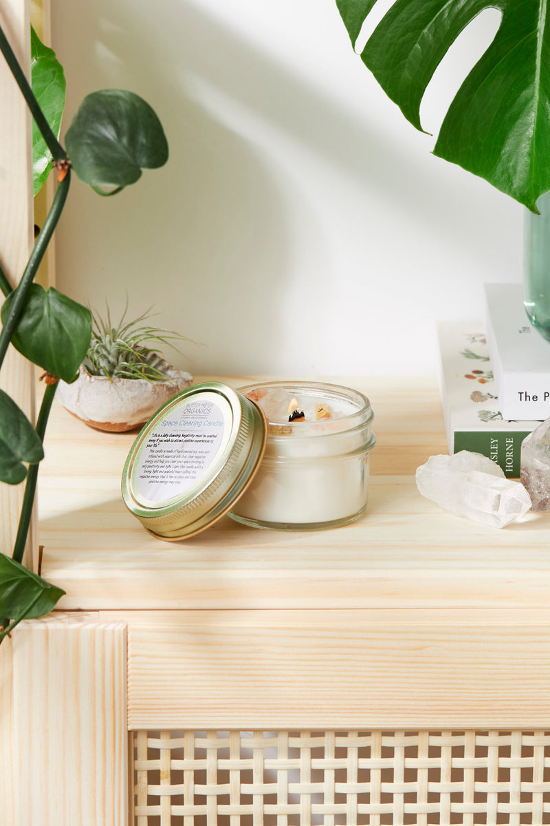 Organic soy space clearing candle with crystals on a shelf, surrounded by plants and books.
