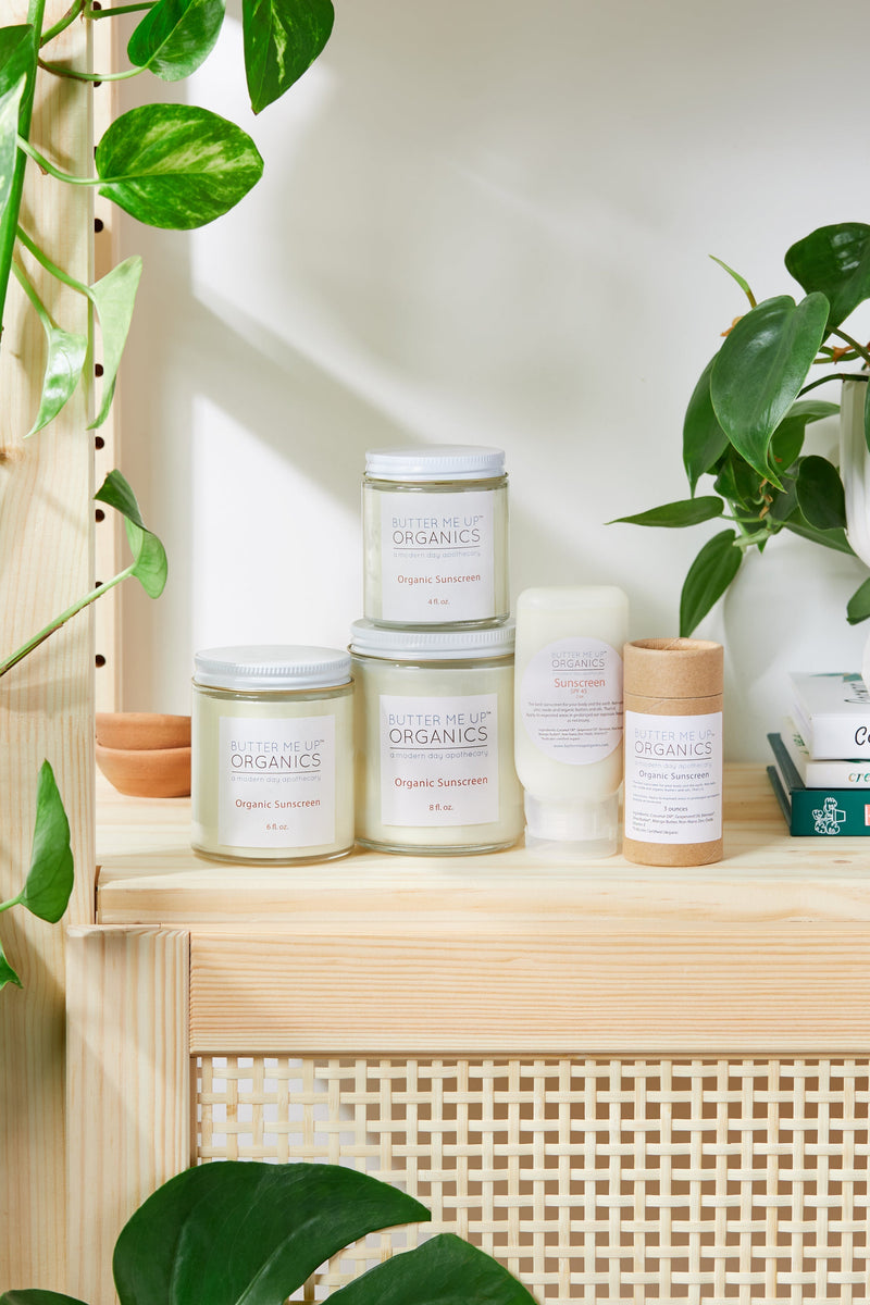 Natural organic sunscreen jars and containers on a wooden shelf surrounded by green plants.