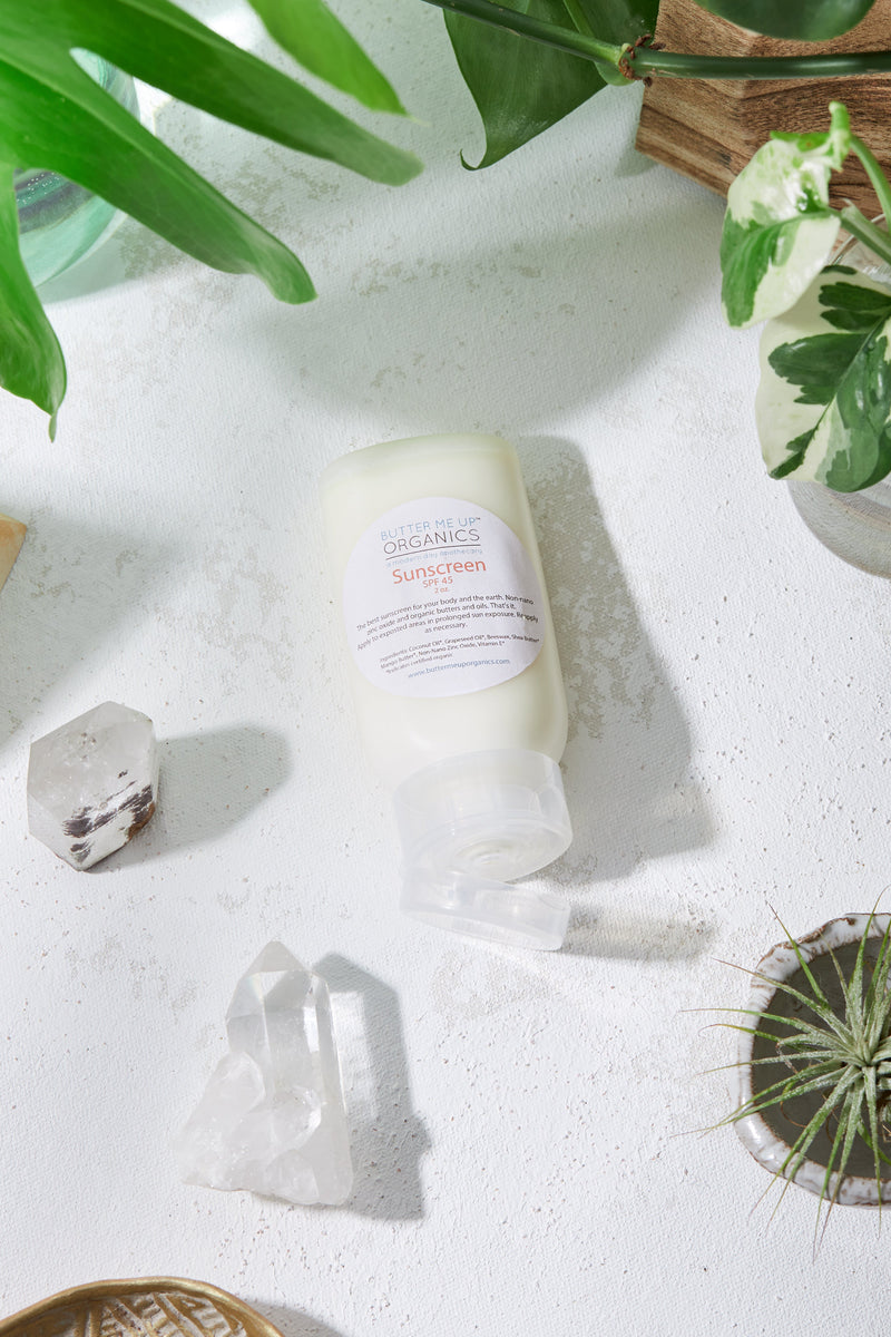 Natural organic sunscreen with non-nano zinc oxide for SPF 45 protection, shown in a squeeze bottle on a white surface surrounded by plants and crystals.