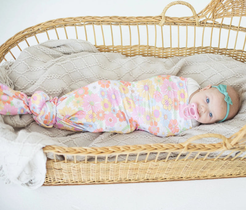 Buttery soft and stretchy retro floral swaddle blanket enveloping a baby in a wicker basket.
