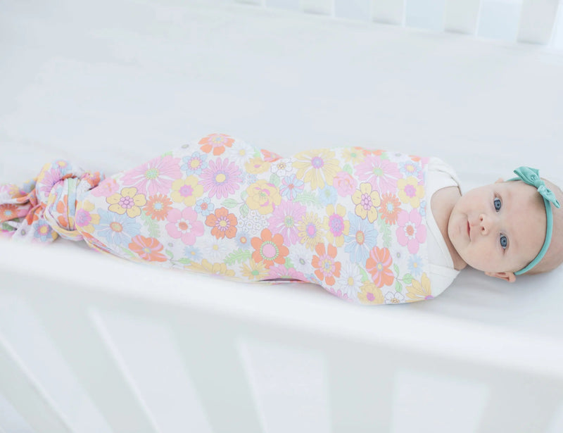 Buttery soft and stretchy swaddle blanket in retro floral design covering a baby in a crib.