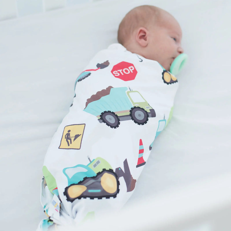 Baby wrapped in buttery soft and stretchy swaddle blanket with construction trucks design.
