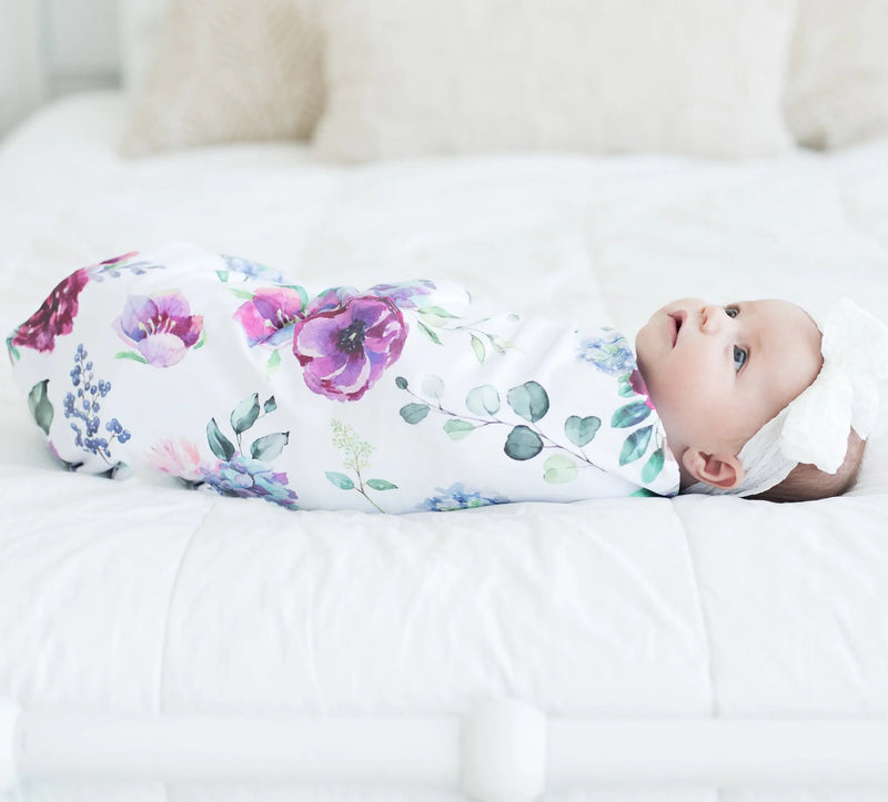 buttery soft and stretchy blue floral swaddle blanket with baby lying on white bed