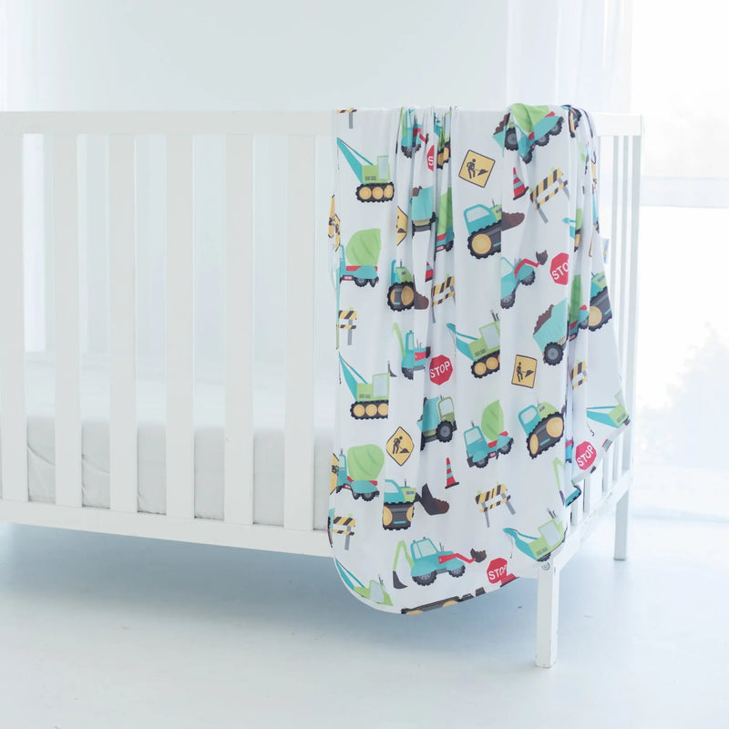 Buttery soft and stretchy swaddle blanket with construction trucks design on crib.