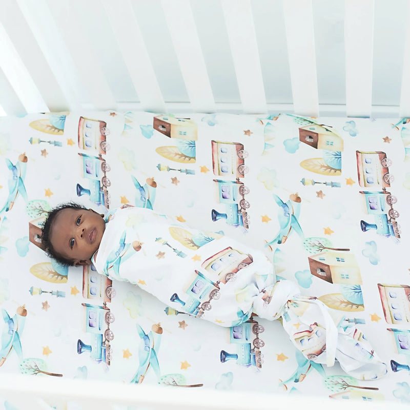 Baby wrapped in buttery soft and stretchy airplane and train patterned swaddle blanket in crib.