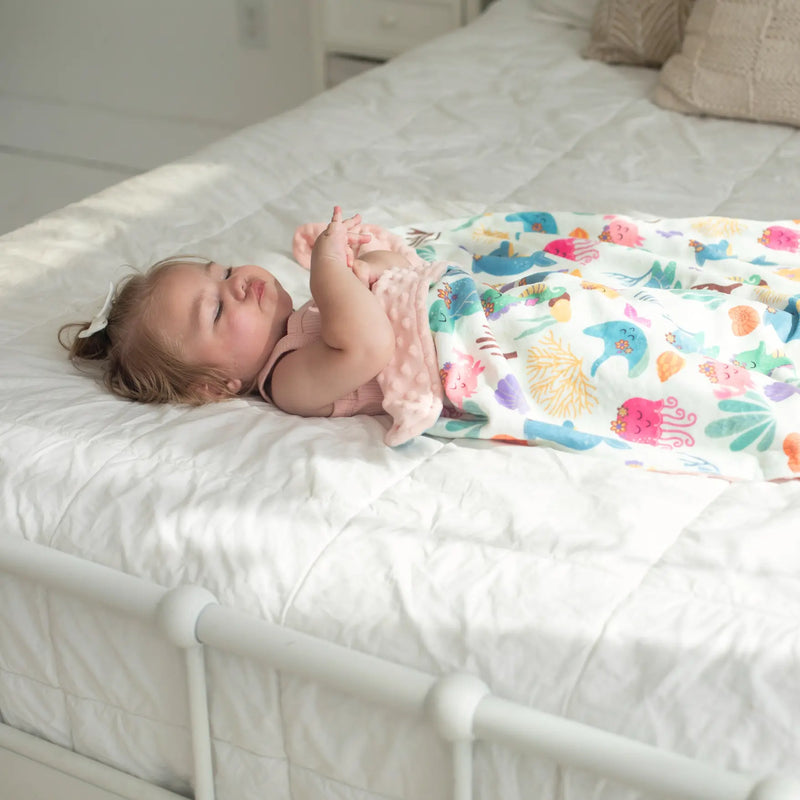 Baby enjoying soft undersea adventure minky blanket on bed.