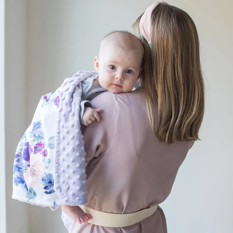 Baby held with a premium floral blanket, showcasing its soft, lightweight design with vibrant purple and blush colors.