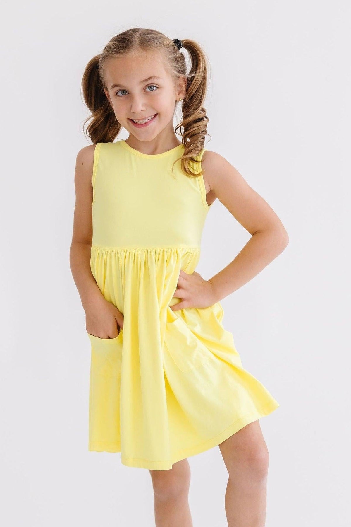 Yellow sleeveless twirl dress with pockets and a scoop back, worn by a smiling young girl