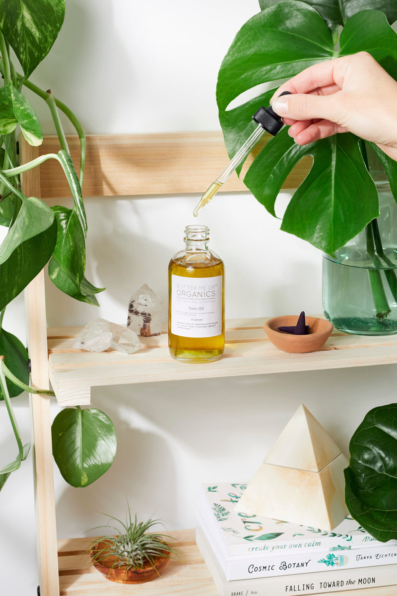 Organic Yoni Oil bottle with dropper on a wooden shelf surrounded by plants and crystals.