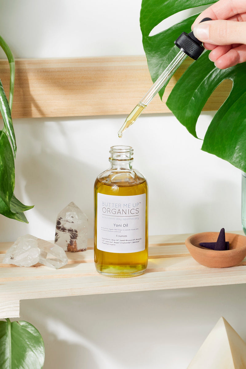Organic Yoni Oil bottle with dropper placed on a wooden shelf, surrounded by plants and crystals.