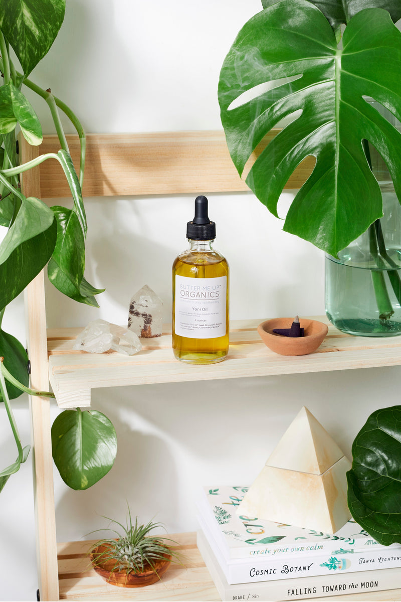 Organic Yoni Oil bottle on a wooden shelf with plants and decorative items.