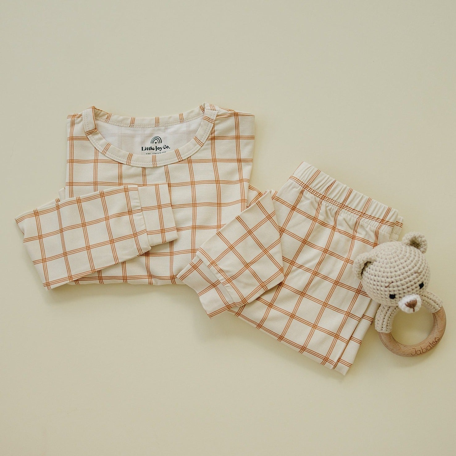 Two-piece baby pajama set in burnt orange plaid with long sleeves and pants