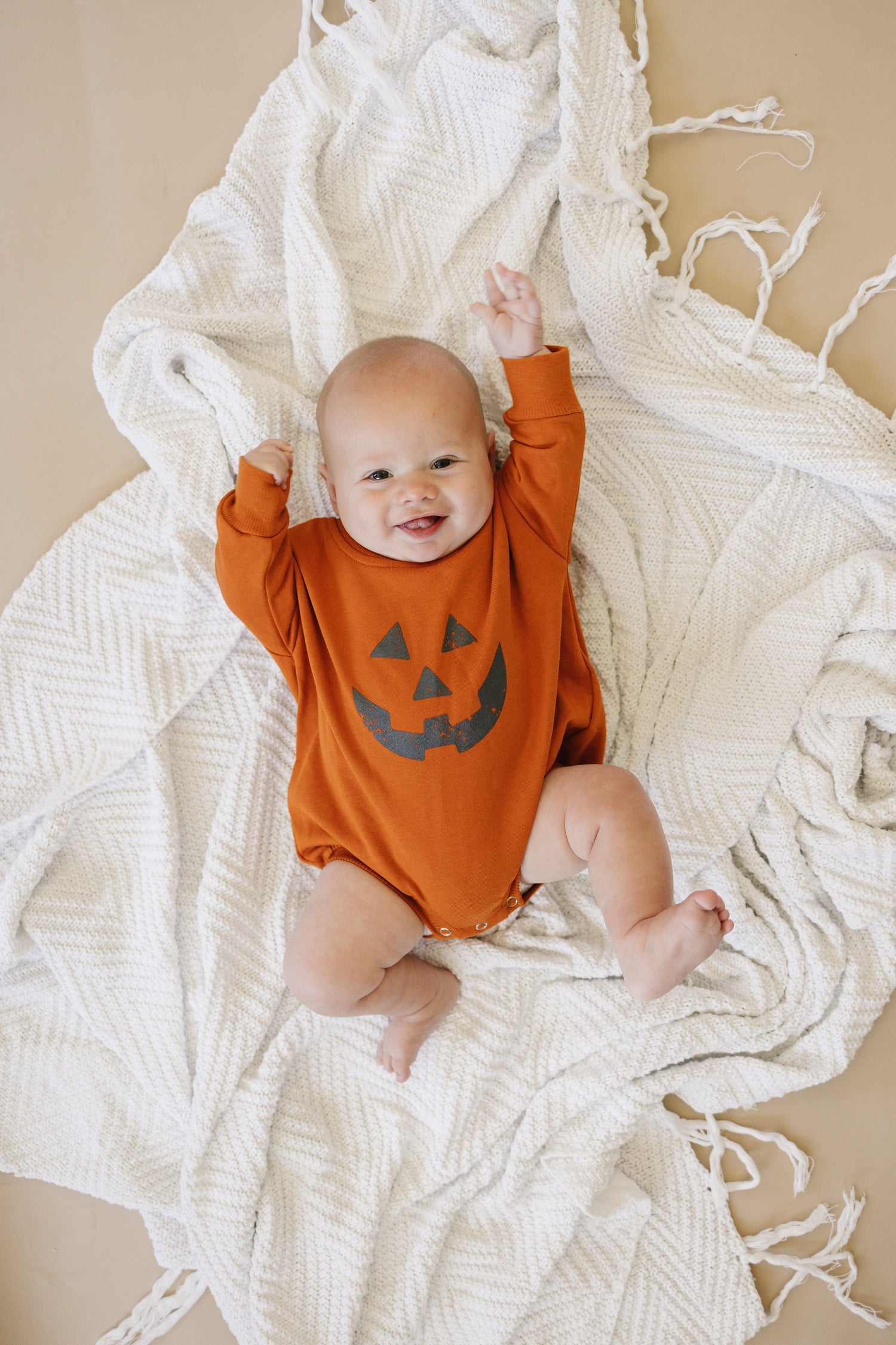 Baby sweatshirt romper with a Jack O Lantern pumpkin graphic and snap closure at the crotch.