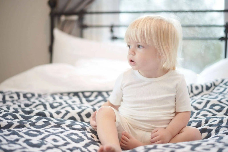 Toddler sitting on bed with Moroccan Blue Newcastle Classics cotton muslin blanket.