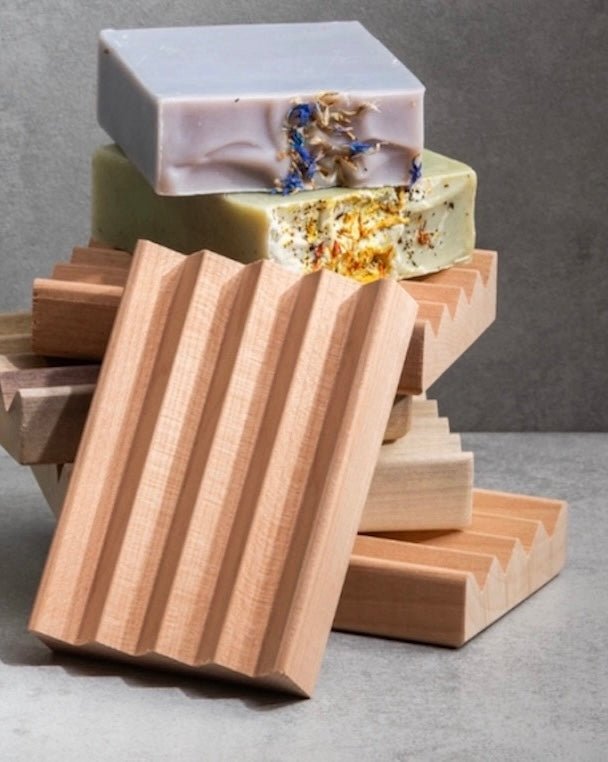 Close-up of a natural, untreated alder wood soap dish with visible grain, holding a bar of soap.