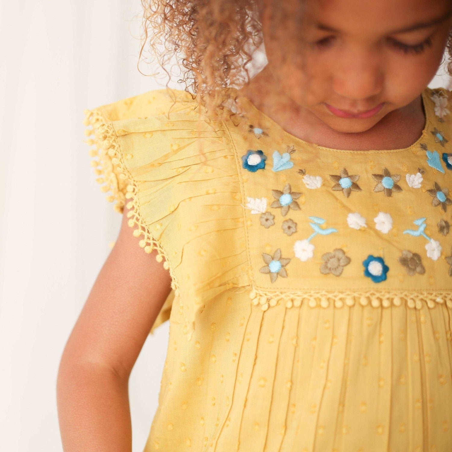 Mustard mini dress with embroidery and pom pom trim along the hem.