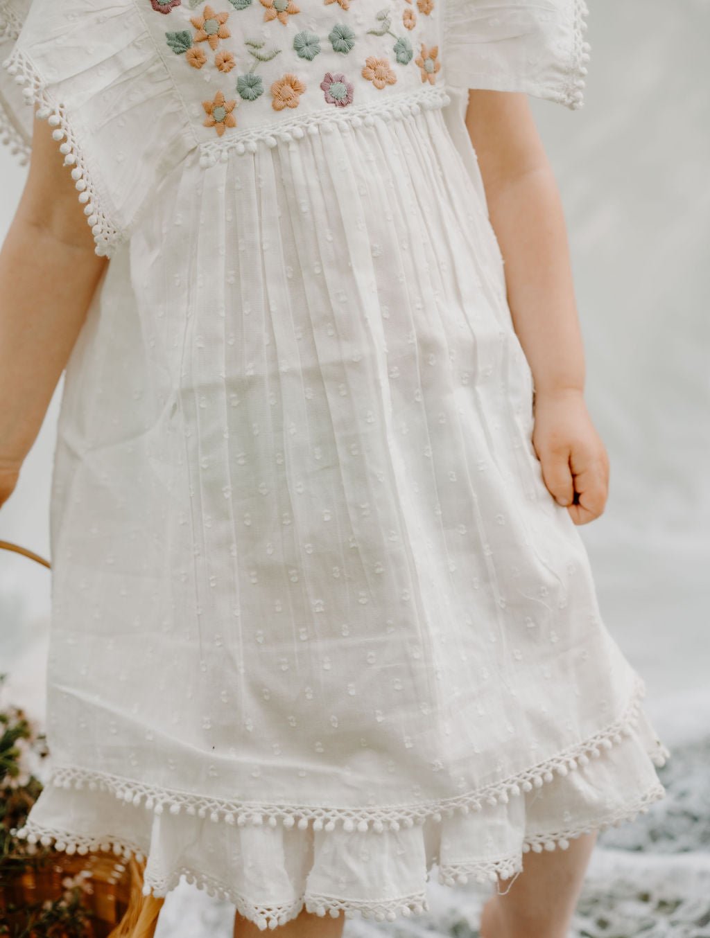 White mini dress with embroidery detailing and pom pom trim along the hem.