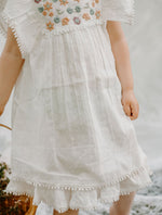 White mini dress with embroidery detailing and pom pom trim along the hem.
