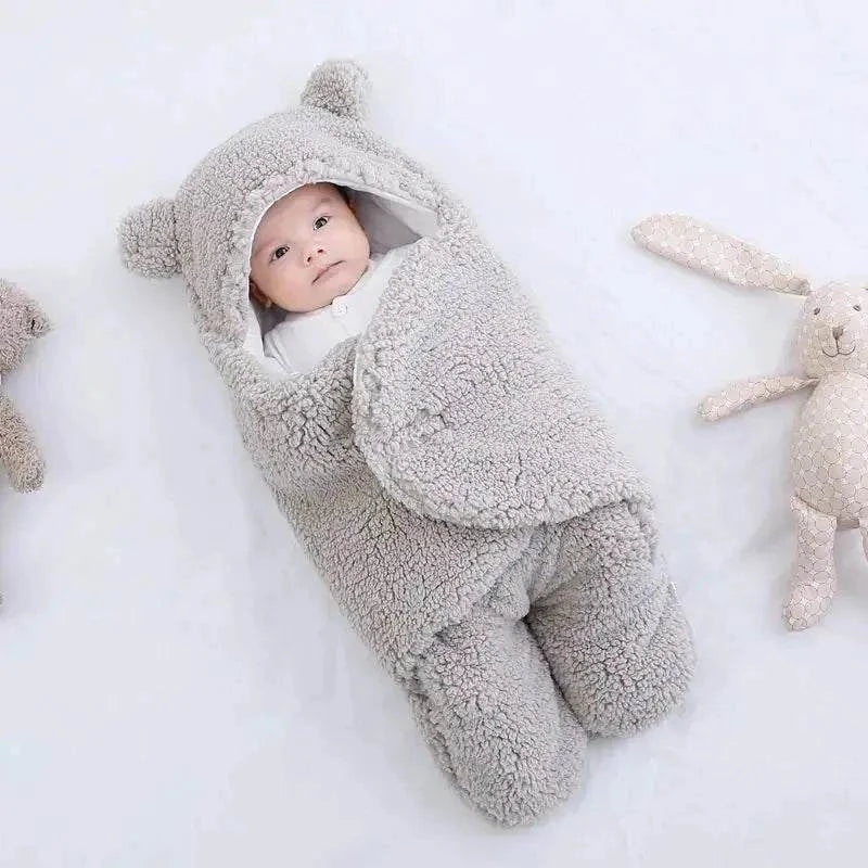 Baby in gray fleece sleeping bag with plush toys nearby.