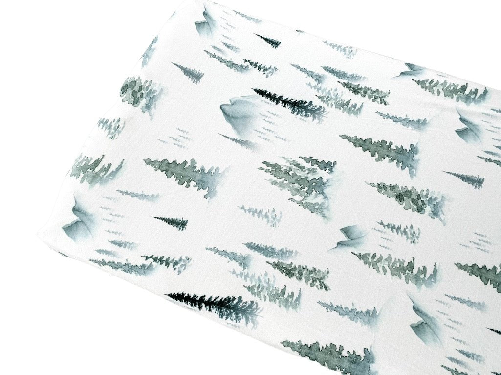 Soft organic bamboo changing pad cover in a green forest print, draped over a changing pad.