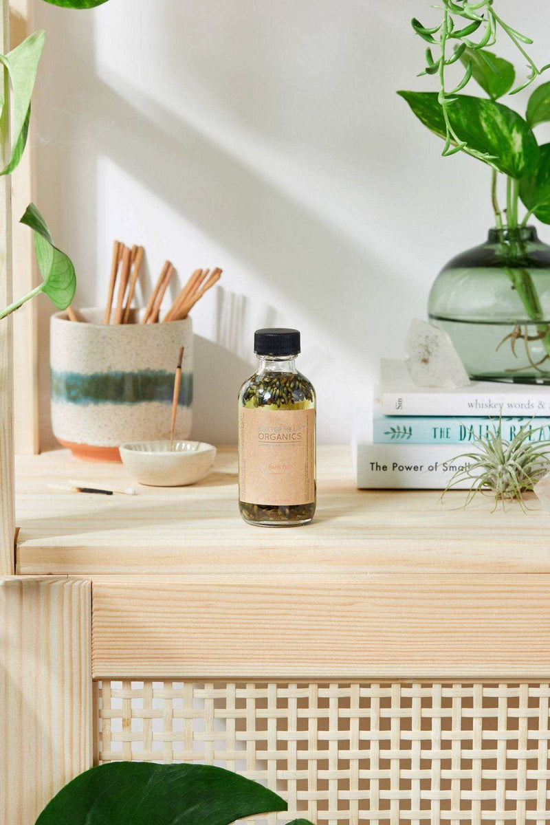 Bath Oil with Relaxing Lavender in a 2oz bottle on a wooden shelf with plants and books.