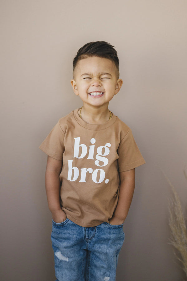 Toddler wearing a "Big Bro" graphic t-shirt and jeans, smiling and laughing.