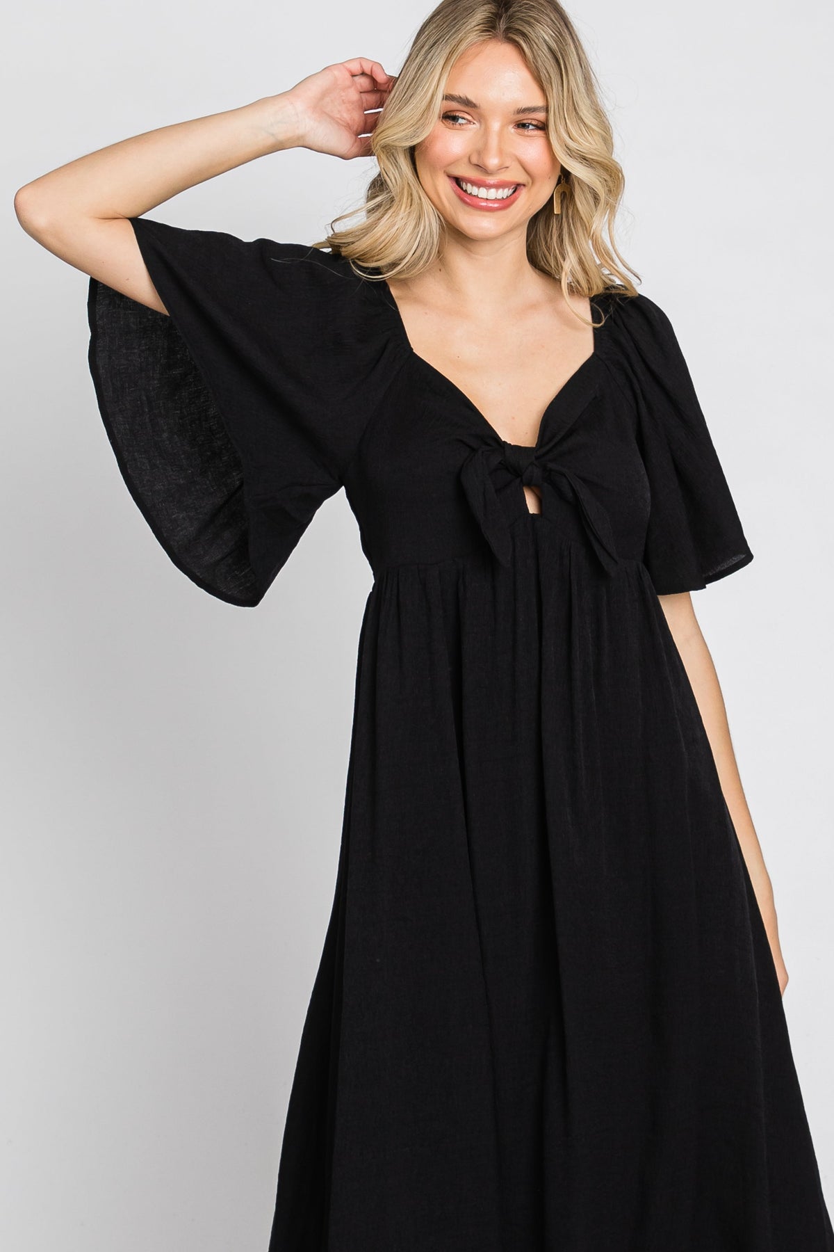 Woman models a black ruffle sleeve midi dress with a front tie detail, looking elegant.