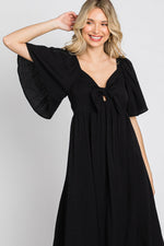Woman models a black ruffle sleeve midi dress with a front tie detail, looking elegant.