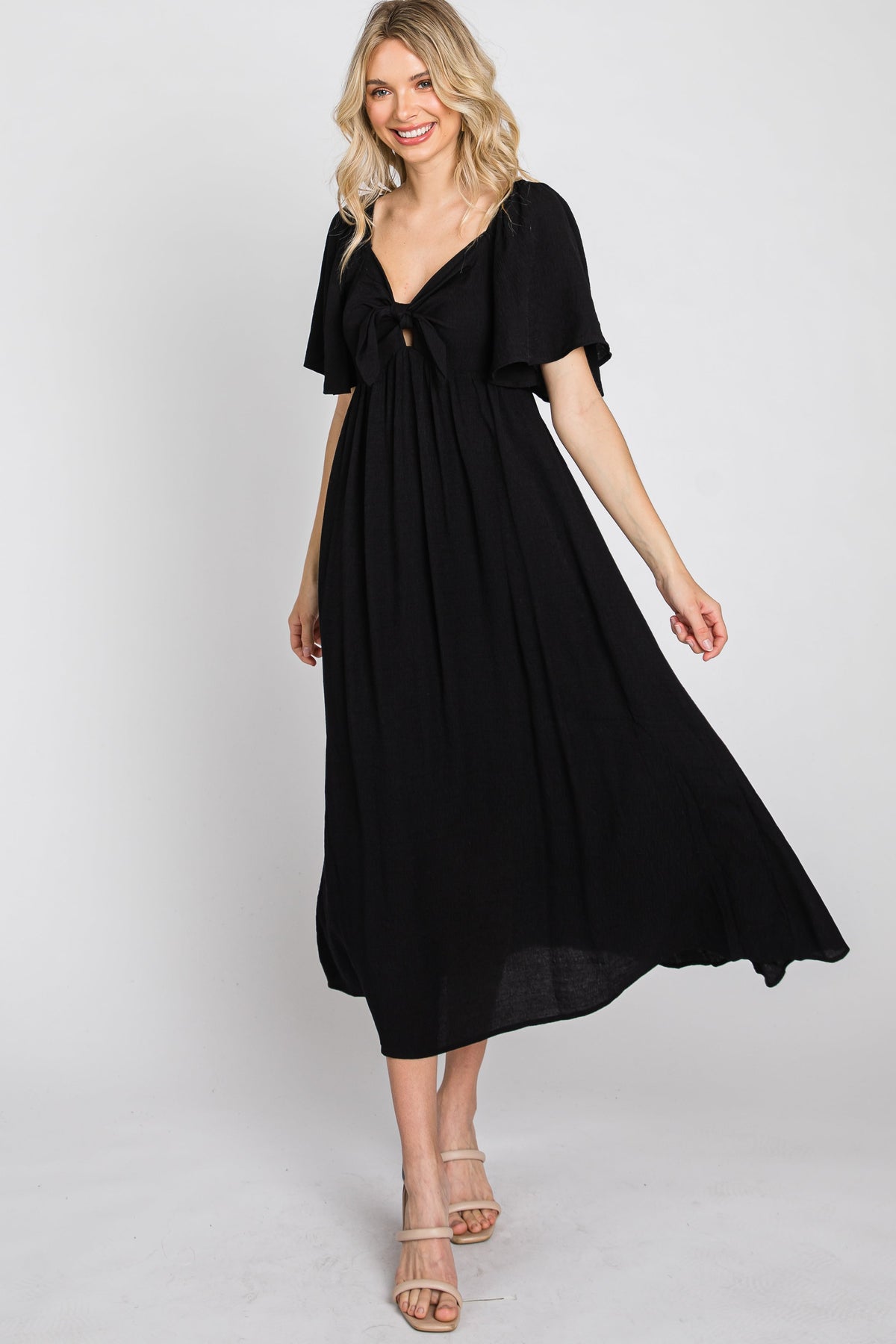 Woman models a black ruffle sleeve midi dress with a front tie detail, looking elegant.